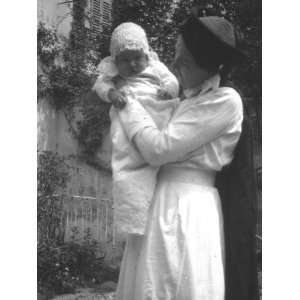  A Baby Boy in a Long White Dress Being Held by His Nurse 